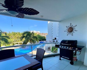 Un balcon avec vue sur une piscine, un barbecue et une chaise.