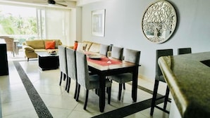 Un comedor con una mesa dispuesta para cuatro personas, rodeada de sillas. Se aprecia un sofá y una mesa de centro al fondo.
