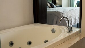Un baño moderno con una bañera grande, un espejo y vistas a un dormitorio con cama y mesita de noche.