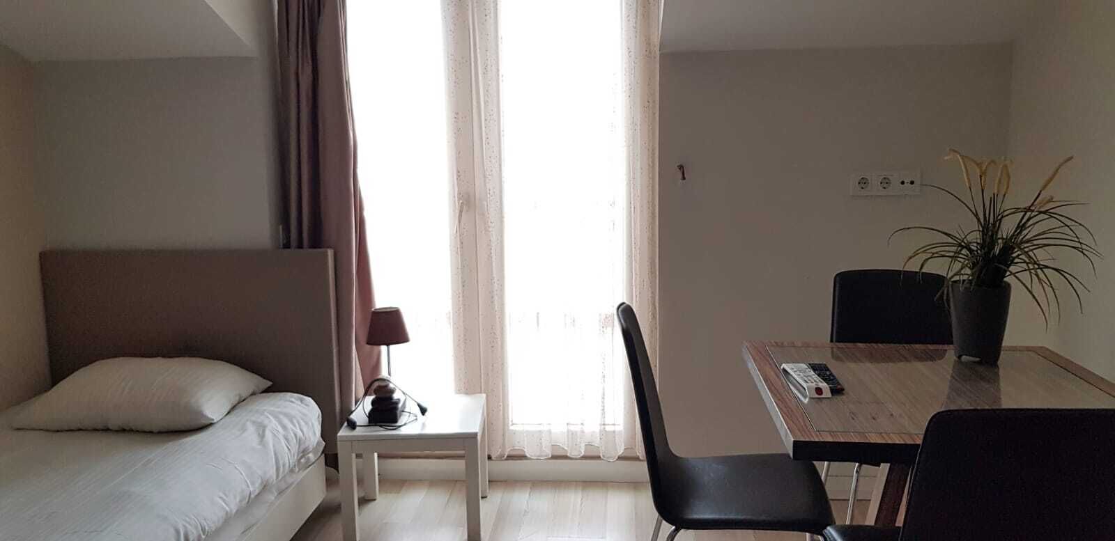 Ein Hotelzimmer mit einem Bett, einem kleinen Tisch mit Lampe, einem Sessel, einem Schreibtisch mit Computer und einer Zimmerpflanze.