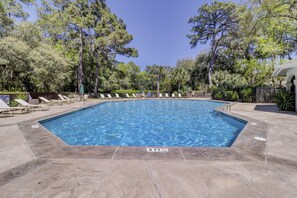 Une piscine rectangulaire à l’eau d’un bleu limpide, entourée de chaises longues et d’un panneau indiquant la présence d’un sauveteur.