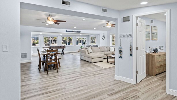 A spacious living room with a dining area, wooden flooring, ceiling fans, and large windows. - Our piece of paradise! (Weeki Wachee)