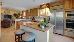 A modern kitchen with a central island, stainless steel appliances, and a dining area with a leather couch.