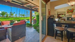 A modern outdoor bar area with wicker furniture, a pool, and a view of a golf course.