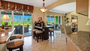 A spacious kitchen with a bar area, large windows, and a view of a tropical landscape.