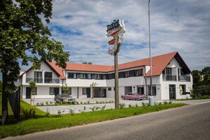 A two-story motel with a red roof, a signboard, and a parking area with cars. - Motel Eldorado (Mikulov)