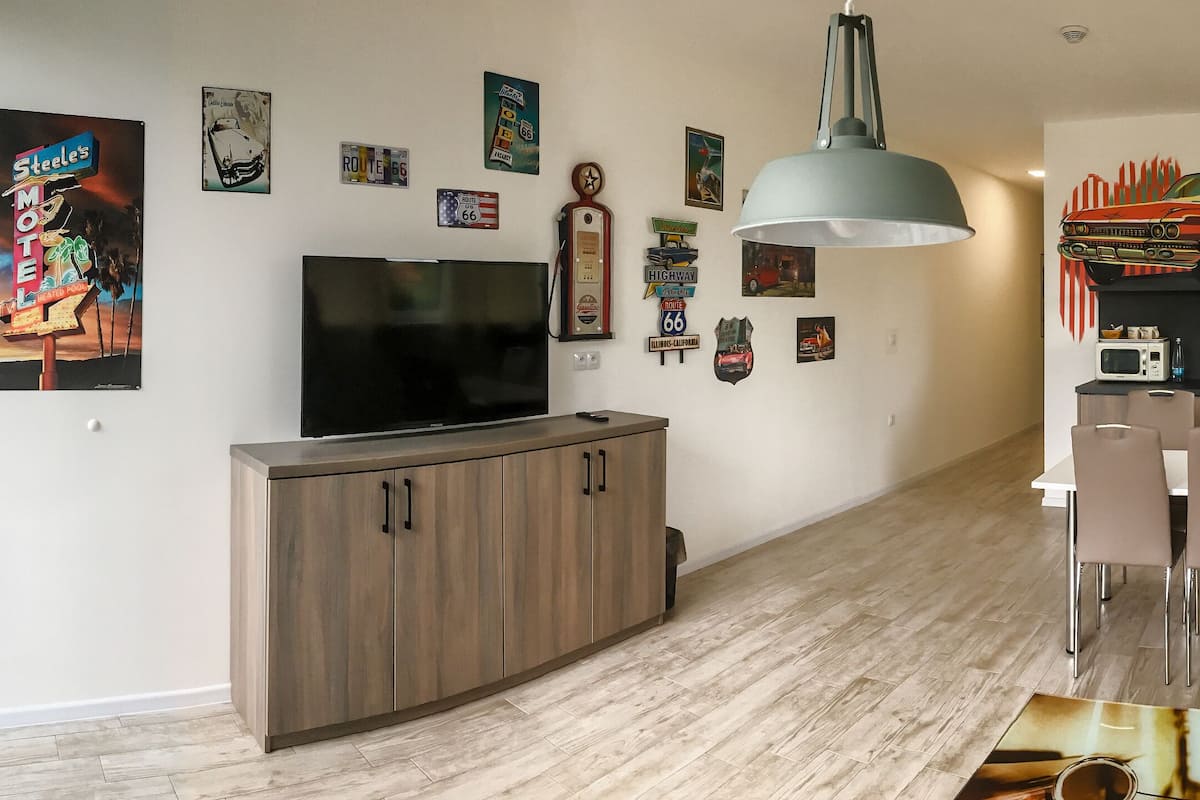 A modern living room with a flat-screen TV, wooden cabinets, and a dining area with chairs and a table.