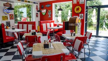 Un restaurante con asientos y mesas rojas, letreros antiguos de Chevrolet y un jukebox.