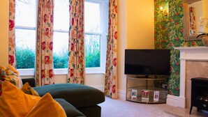 Ein Wohnzimmer mit Sofa, Fernseher, Kamin und floralem Wandpapier.