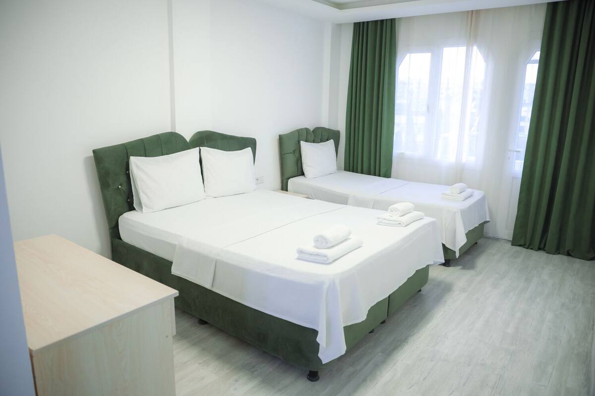 A hotel room with two beds, a desk, and a view of the city through the window.