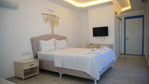 A bedroom with a bed, bedside tables, a TV, and a door. - Hotel Angel Beach (Erdemli)
