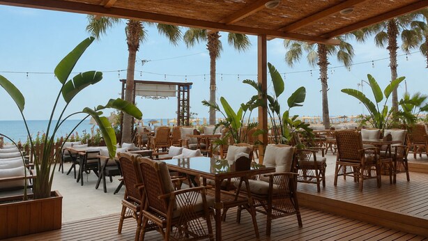 An outdoor dining area with wicker furniture, a wooden deck, and a view of the sea. - Hotel Angel Beach (Erdemli)