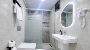 A modern bathroom with a toilet, shower, sink, and a hairdryer mounted on the wall. - Hotel Angel Beach (Erdemli)