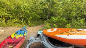 Des kayaks et une planche à pagaie près d’un sentier forestier.