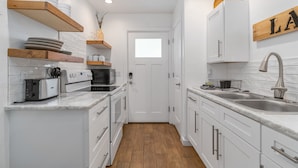 Una cucina moderna con mobili bianchi, scaffali in legno, un tostapane, un forno e un lavello.