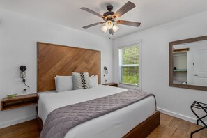 A bedroom with a large bed, wooden headboard, ceiling fan, bedside lamps, and a window with blinds. - GrandLake*Kayak*ForestView*Firepit*Kings*Lakefront (Grove)