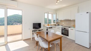 Una cocina moderna con armarios blancos, una mesa de comedor con sillas, horno empotrado y un amplio ventanal con vistas a una colina verde.