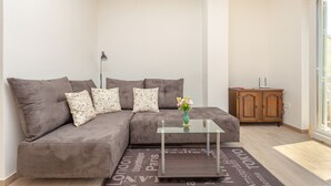Una sala de estar moderna con un sofá seccional gris, una mesa de centro de vidrio, una lámpara de pie y un mueble de madera.
