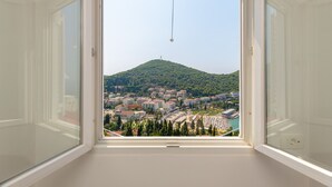 Vista desde una ventana de marco blanco, con vista a un pueblo con edificios, una colina y un cielo despejado.