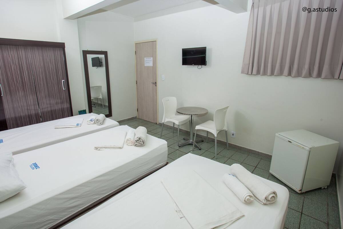 Habitación de hotel con dos camas, una mesita, una silla, un televisor y un refrigerador pequeño.