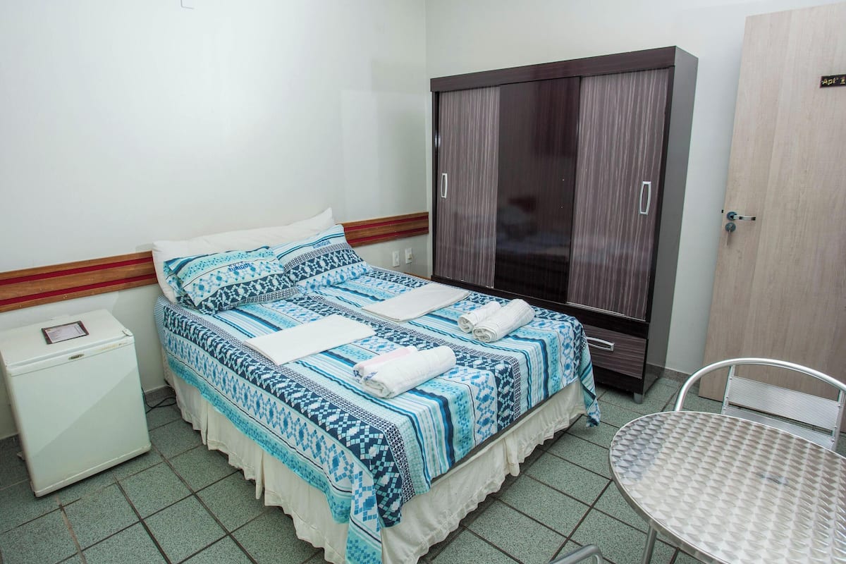 Un dormitorio con cama, armario, mesita de noche y una pequeña mesa.