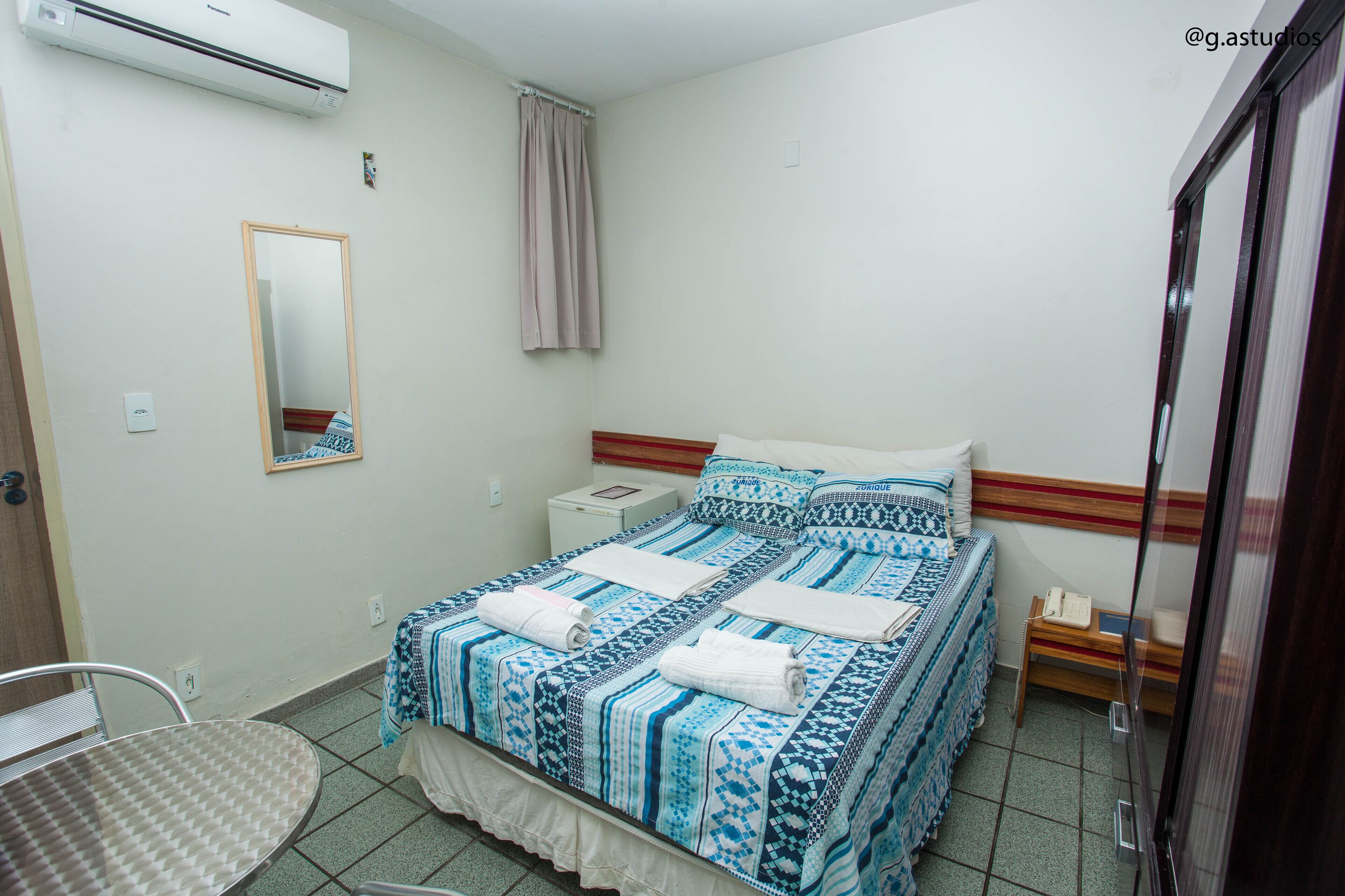 Een slaapkamer met een bed, nachtkastje, stoel, spiegel en een airconditioning.