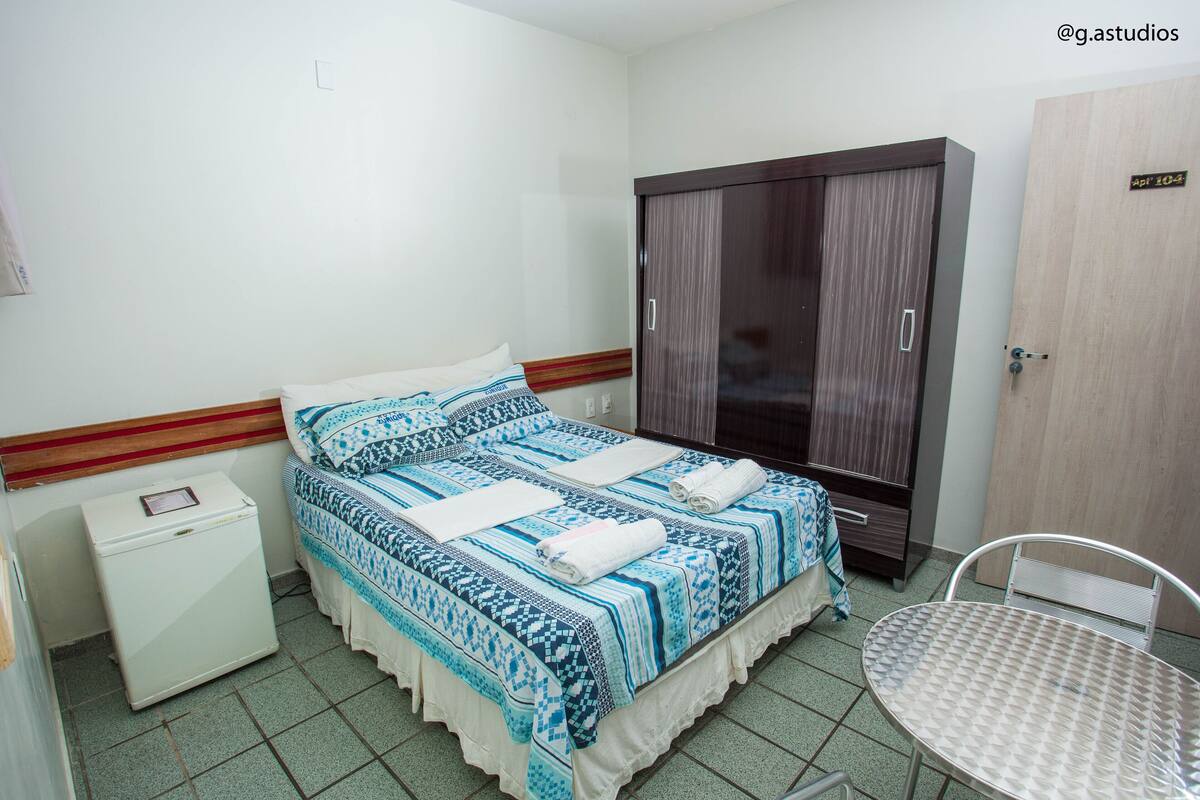 Un dormitorio con cama, armario, mesita y refrigerador.