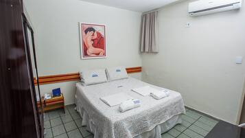 Una habitación de hotel con cama, mesita de noche, unidad de aire acondicionado y un cuadro en la pared.