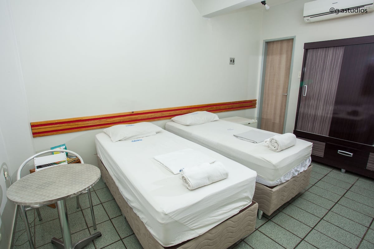 Una habitación de hotel con dos camas individuales, una mesita y un armario.