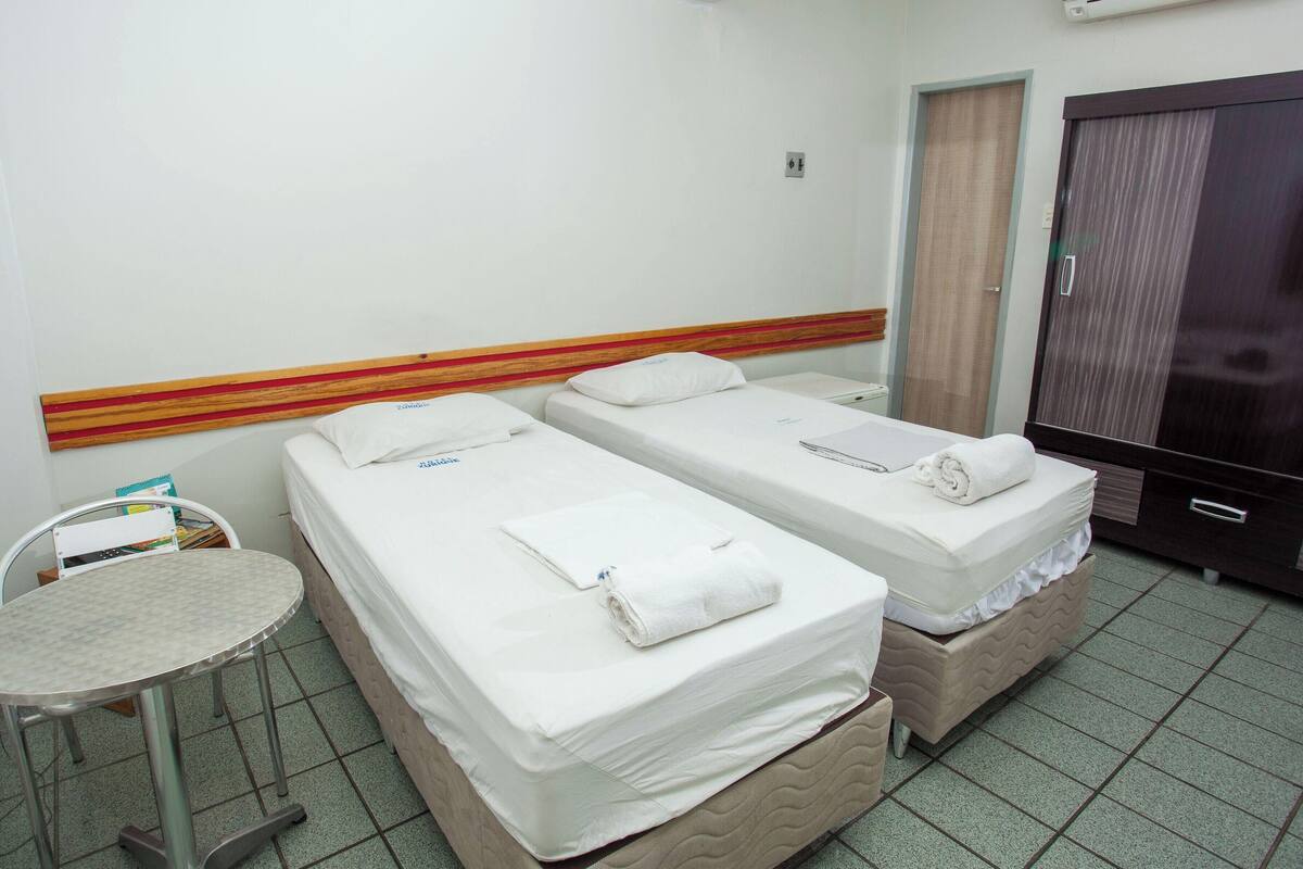 Una habitación de hotel con dos camas individuales, una mesita redonda pequeña, un armario y una puerta.