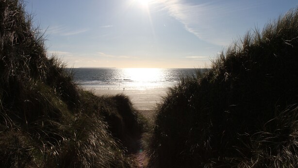 Ein Weg, der zu einem Strand führt, mit tief stehender Sonne am Horizont.