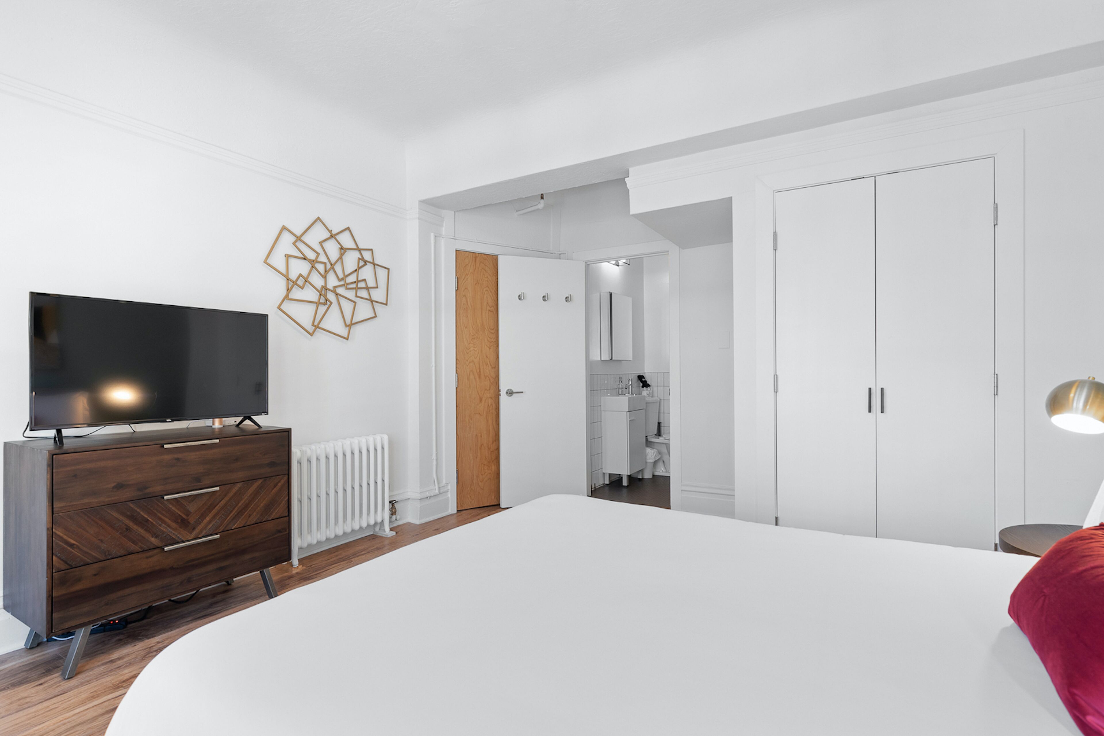 Un dormitorio moderno con una cama grande, un televisor, un aparador de madera y un armario blanco.