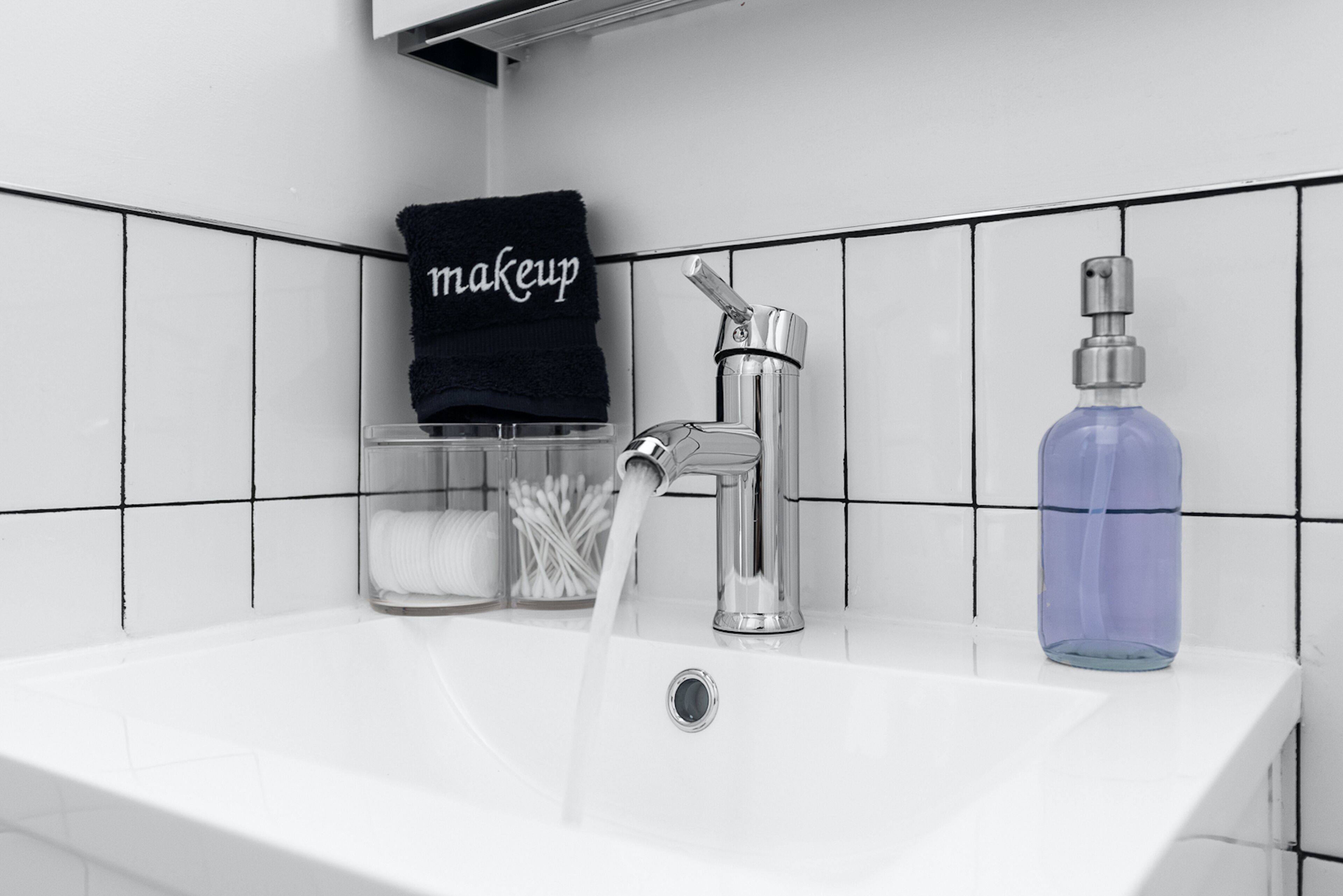A bathroom sink with a faucet, a bottle of hand soap, and a towel rack with a towel labeled "makeup".