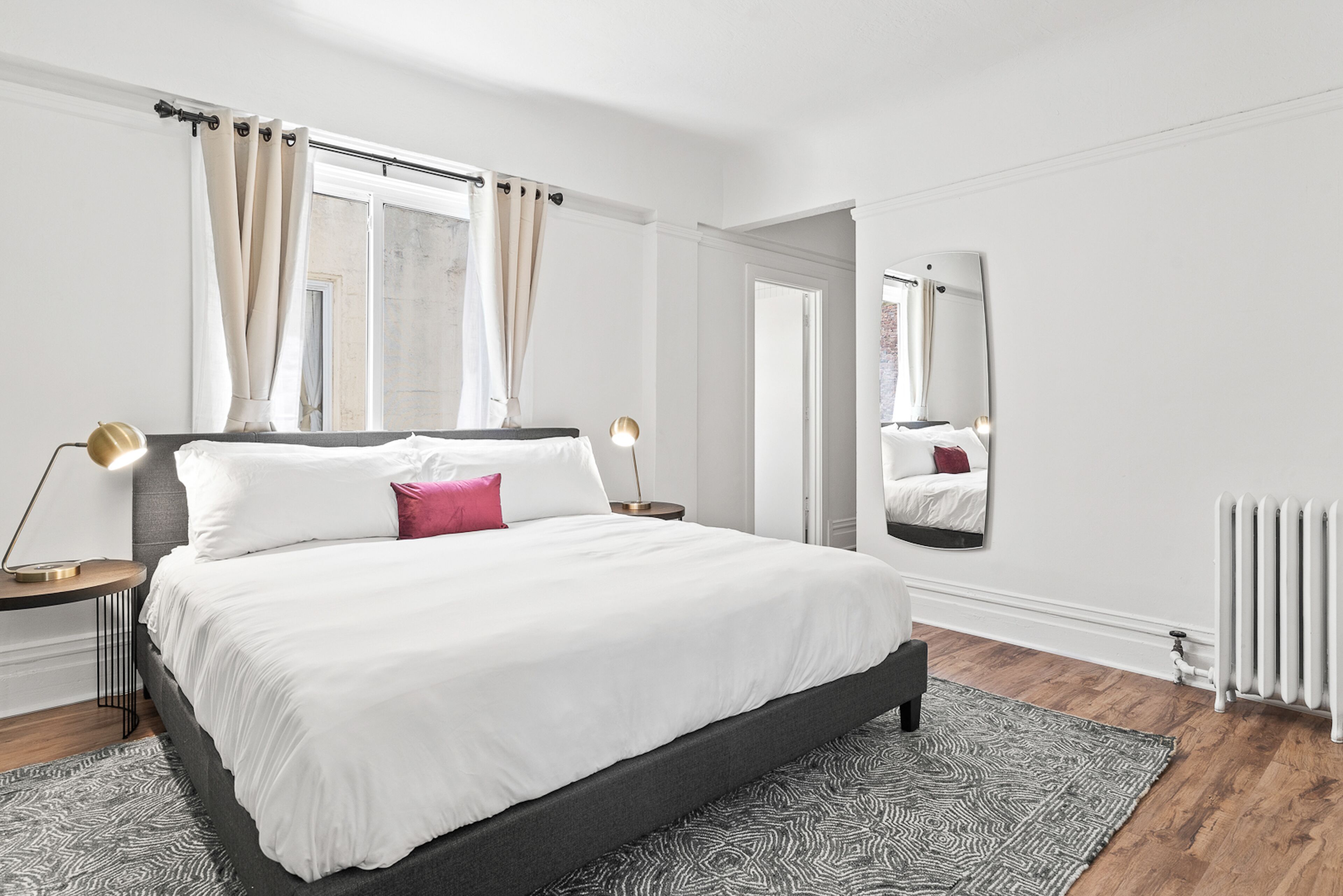 Une chambre à coucher moderne avec un grand lit, une table de chevet avec une lampe, un miroir et un radiateur.