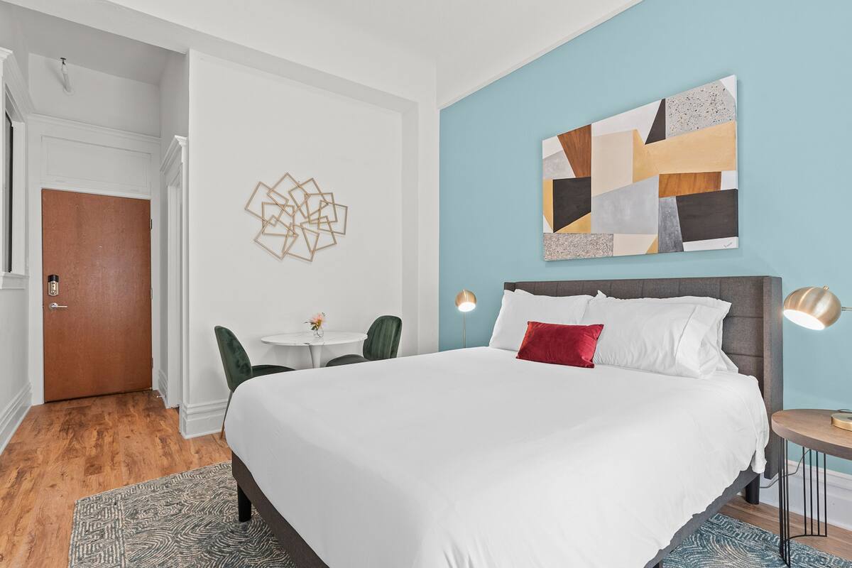 Une chambre d’hôtel avec un grand lit, un bureau, une chaise, une œuvre d’art murale et une porte.