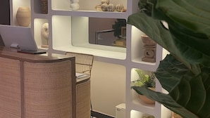 A reception desk with a laptop, a plant, and a wall with shelves displaying decorative items. - Moet Medellin Hotel (Medellín)