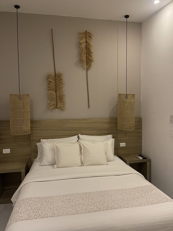 A neatly made bed with a patterned bedspread, two bedside tables with lamps, and decorative feathers hanging from the ceiling.