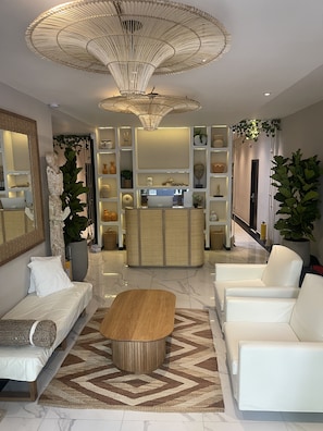 A modern living room with a sofa, two white armchairs, a wooden coffee table, and a large decorative light fixture. - Moet Medellin Hotel (Medellín)