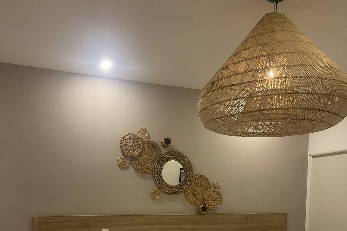 Ein Schlafzimmer mit einem Holz-Kopfteil, einem großen Bett mit weißer Bettwäsche, einer gewobenen Leuchte und einem wandmontierten Spiegel.