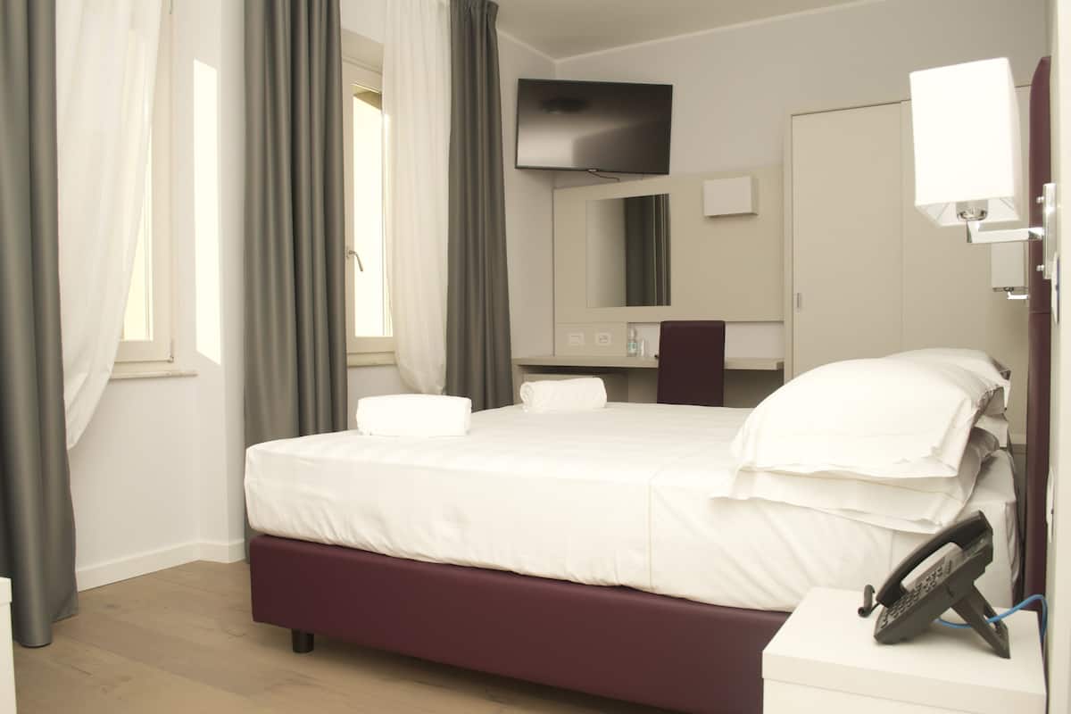 A hotel room with a bed, a TV, a bedside table, and a telephone.