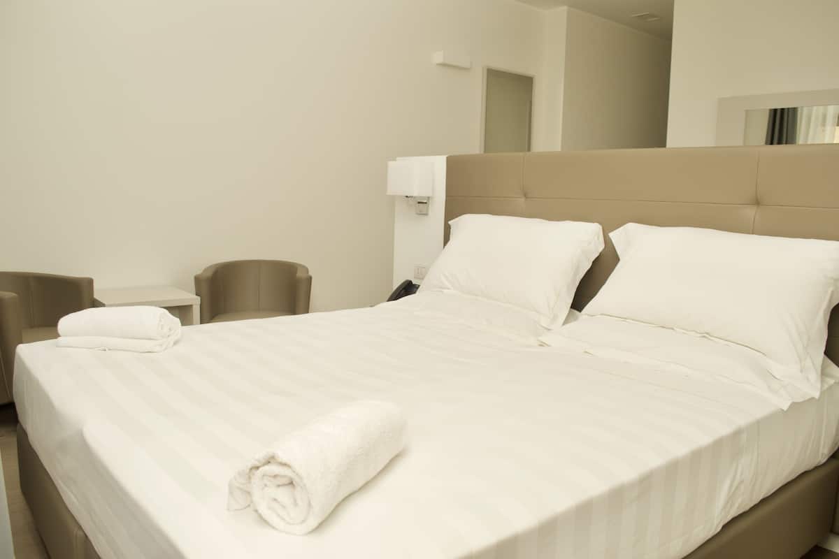 A hotel room with a large bed, a bedside table, a lamp, and a mirror on the wall.