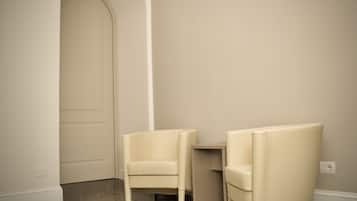 Una habitación con dos sillones blancos, suelo de mármol y una pared lisa con una puerta.