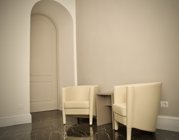 A room with two white armchairs, a marble floor, and a plain wall with a door.