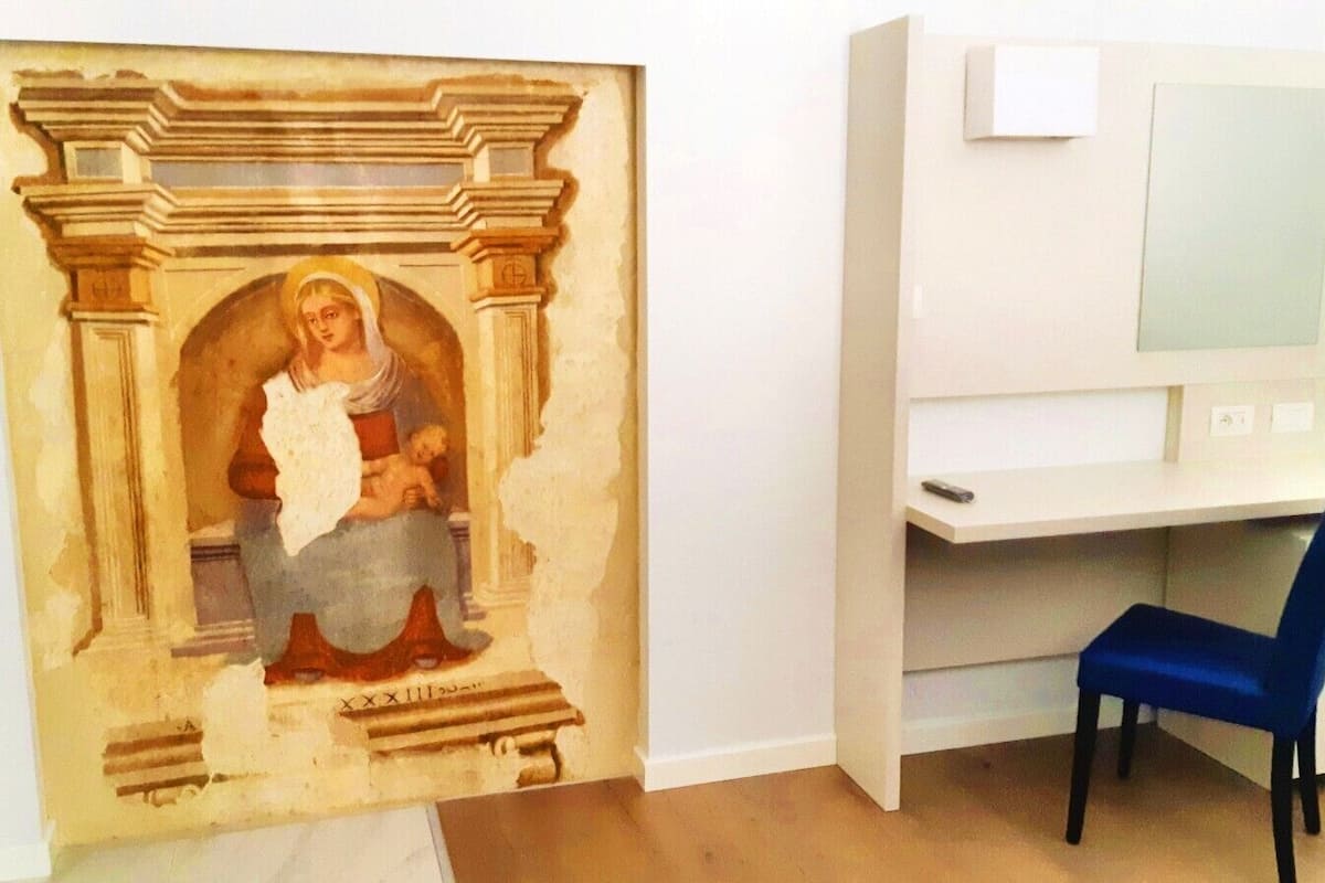 A room with a white desk, a blue chair, and a partially visible painting on the wall.