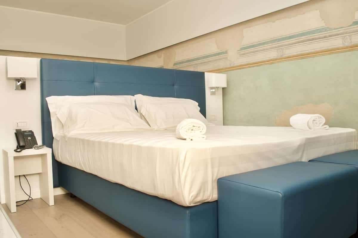 A modern hotel room with a large bed, a bedside table with a phone, and a small seating area.