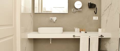 Un baño moderno con un lavamanos blanco, un espejo, un secador de pelo y un cubo de basura.