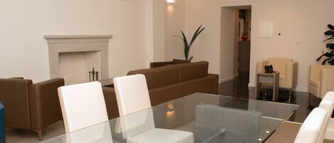 A modern living room with a glass coffee table, brown leather sofas, and a fireplace.