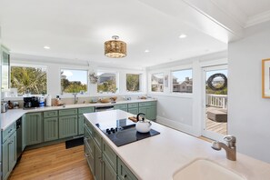 A modern kitchen with green cabinets, a large island, and a view to the outdoors.