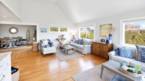 Uma sala de estar espaçosa com teto alto, piso de madeira e grandes janelas com vista para o exterior.
