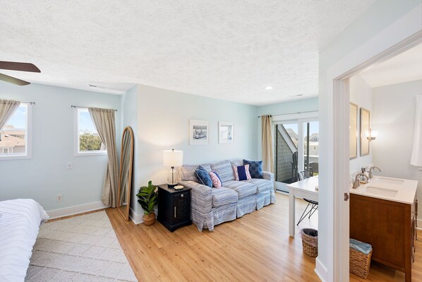 A modern bedroom with a bed, a bedside table, a lamp, a sofa, and a view of the outside.